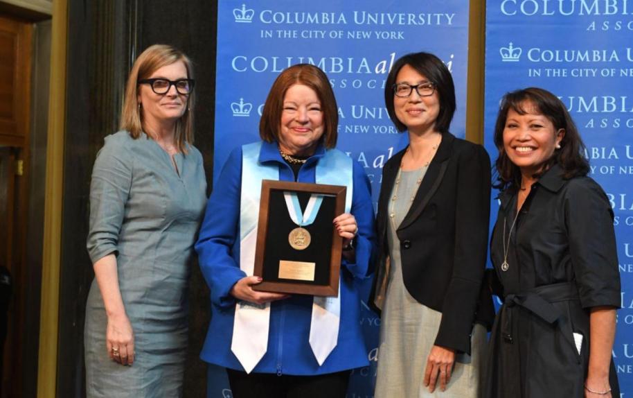 Four smiling alumnae with one in regalia holding a 2022 CAA Alumni Medal after medalist ceremony